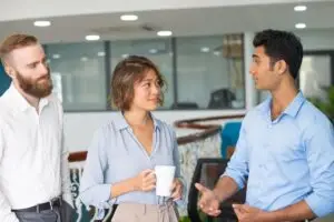 Employees meeting and chatting during lunch break. Three workers talking in office space, female employee holding white cup. Networking concept